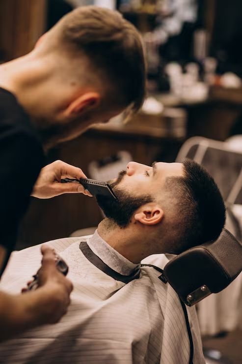 Barbeiro aparando a barba de um cliente reclinado na cadeira